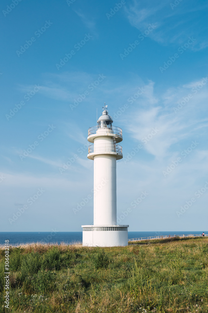 White lighthouse on shoreline in summer