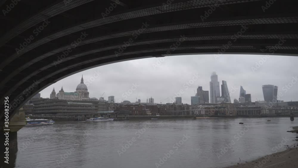 A view of central London underneath a bridge over the Thames River.