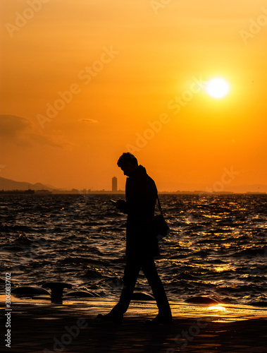 Sea and silhouette at sunset. (Man playing with mobile phone.)