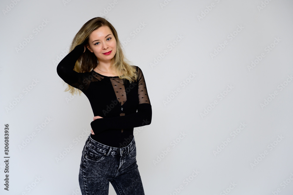 Concept of a woman talking to the camera. A photo of a pretty smiling girl with long beautiful curly hair in a black T-shirt on a white background is standing right in front of the camera. Concept of a woman talking to the camera. A photo of a pretty smiling girl with long beautiful curly hair in a black T-shirt on a white background is standing right in front of the camera.