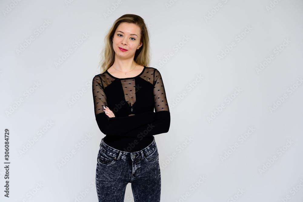 Concept of a woman talking to the camera. A photo of a pretty smiling girl with long beautiful curly hair in a black T-shirt on a white background is standing right in front of the camera. Concept of a woman talking to the camera. A photo of a pretty smiling girl with long beautiful curly hair in a black T-shirt on a white background is standing right in front of the camera.