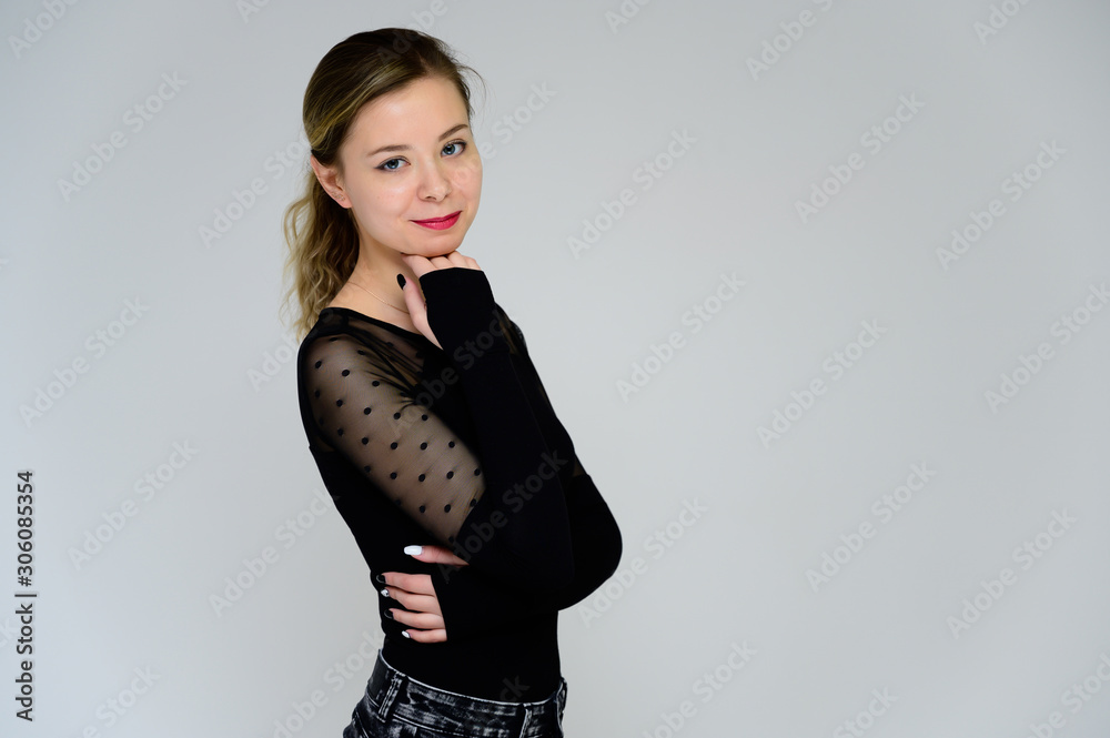 Concept of a woman talking in front of the camera. A photo of a pretty smiling girl with curly hair in a black T-shirt on a white background is standing right in front of the camera. Concept of a woman talking in front of the camera. A photo of a pretty smiling girl with curly hair in a black T-shirt on a white background is standing right in front of the camera.
