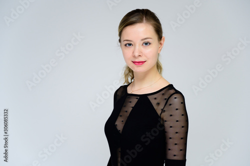 Concept of a woman talking in front of the camera. A photo of a pretty smiling girl with curly hair in a black T-shirt on a white background is standing right in front of the camera.