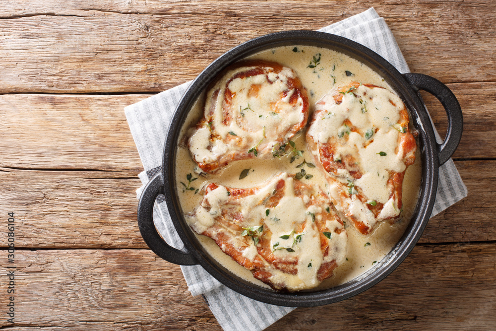 Tasty fragrant pork chops served in a creamy cheese sauce with herbs close-up in a pan. Horizontal top view Tasty fragrant pork chops served in a creamy cheese sauce with herbs close-up in a pan. Horizontal top view