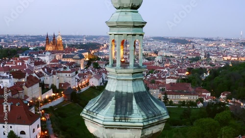 Aerial view cropped steeple of Strahov monastery at night. Cropped view Illuminated belfry lateral motion near towers of ancient cathedral against picturesque panorama above city in twilight photo