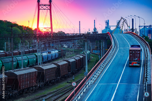 Fototapeta Naklejka Na Ścianę i Meble -  truck with container rides on the road, railroad transportation, freight cars in industrial seaport at sunset