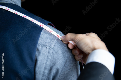 Принти на полотні The dressmaker was measuring the width of the back of the man wearing a blue suit on black background