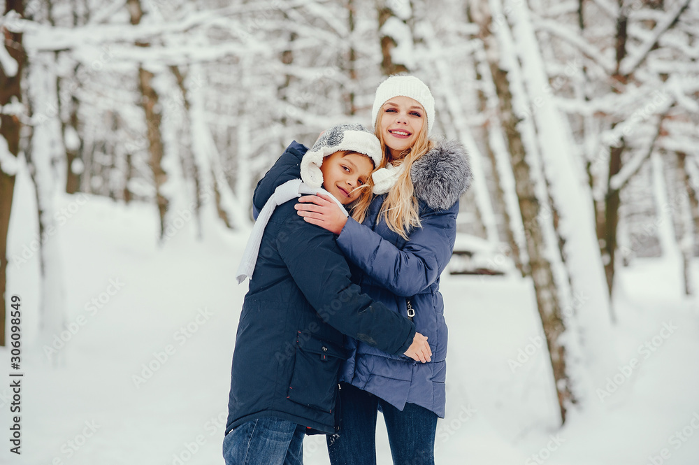 Beautiful mother in a blue jacket. Family playing in a winter park. Little boy in a cute hat Beautiful mother in a blue jacket. Family playing in a winter park. Little boy in a cute hat