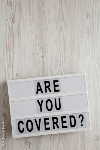 Fototapeta Naklejka Na Ścianę i Meble -  'Are you covered?' words on a modern board on a white wooden background, top view. Overhead, from above, flat lay. Copy space.