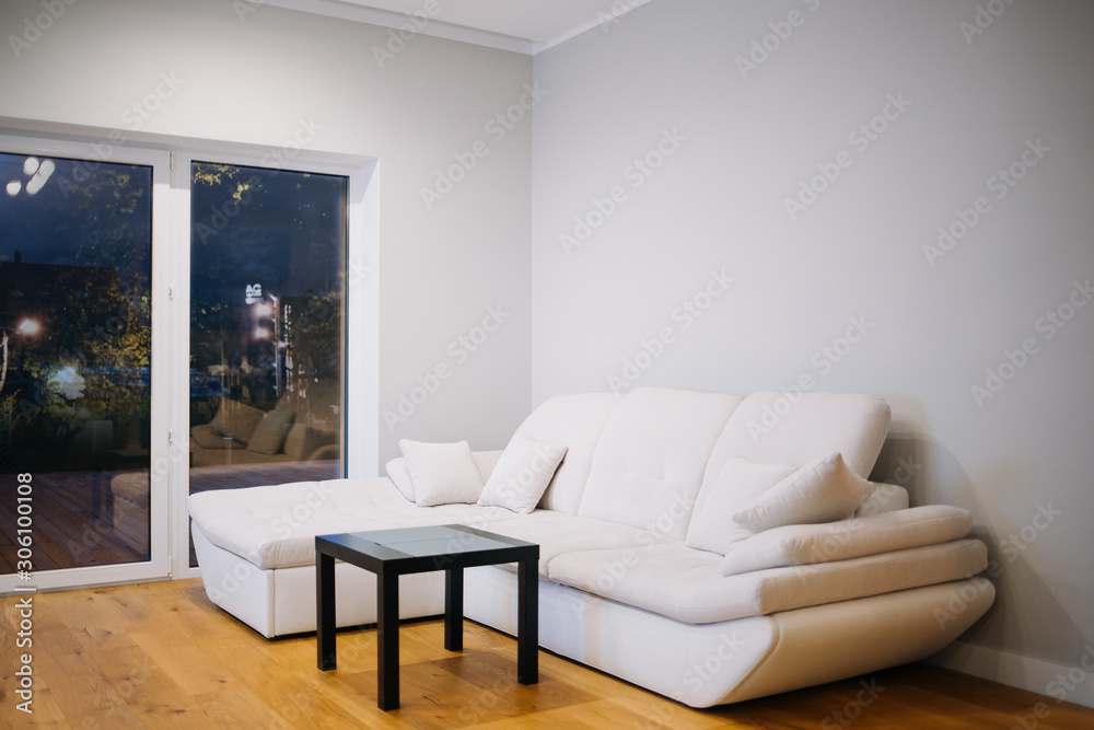 White modern leather sofa against white, empty wall with copy space in simple living room interior White modern leather sofa against white, empty wall with copy space in simple living room interior
