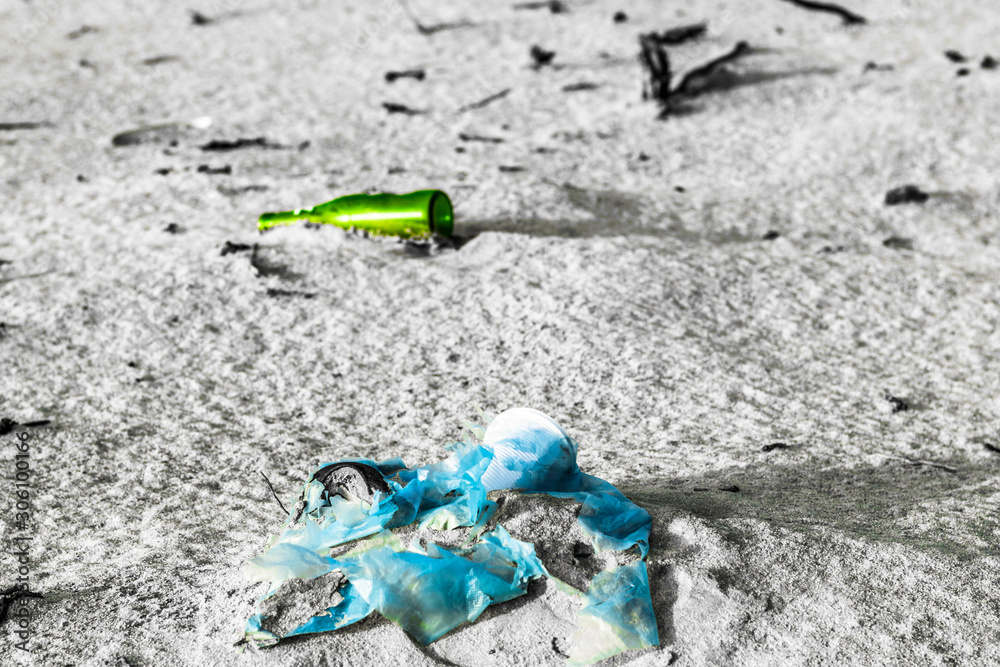 garbage and a glass disposable bottle in the sand at a beach   