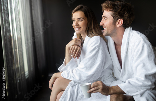 Happy couple in white bathrobes drinking coffee together at morning