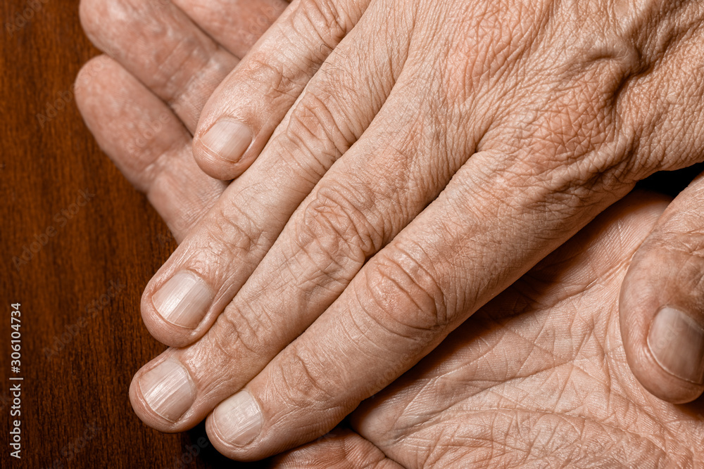 Fototapeta premium Color photo of senior man crossed hands detail on a dark wooden background