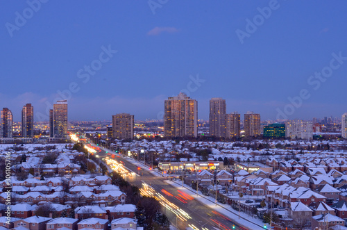 Ariel view of snow covered rooftops of north american neighborhood houses in Mississauga, Ontario, Canada. Light trails of head and tail lights cars going on the highway in the evening photo