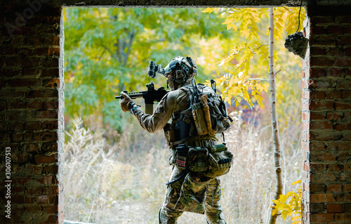 Man in uniform with machine gun between two walls on forest background. Airsoft soldier aims at the sight photo