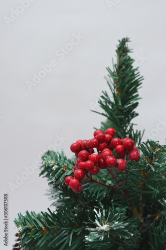 Merry christmas and a happy new year  Green Christmas tree lightly dusted with snow. Plastic Christmas tree on a light background with artificial berries and natural pine cones.