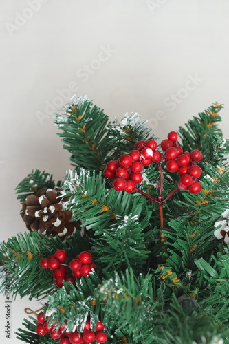 Merry christmas and a happy new year! Green Christmas tree lightly dusted with snow. Plastic Christmas tree on a light background with artificial berries and natural pine cones.