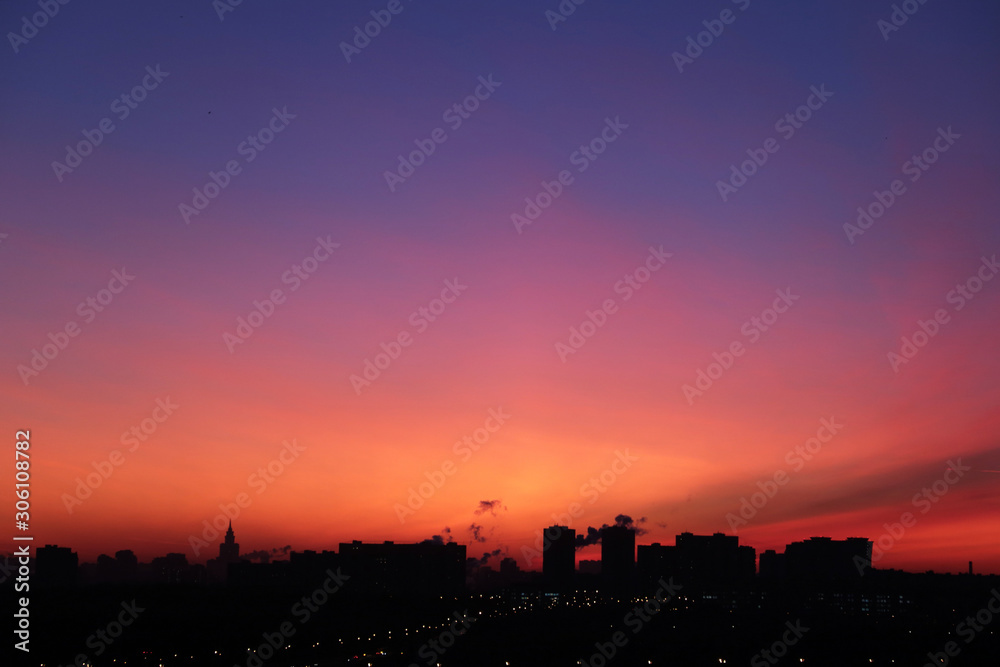 Sunrise over the city, scenic view. Pink-blue sky and cirrus clouds in soft colors above black silhouettes of high-rise buildings, colorful cityscape for background