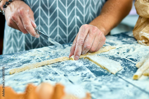 Closeup process making homemade pasta. Chef cook cutting with knife fresh dough for italian traditional pasta to thin ribbon. Italian cuisine recipe. Home cuisine. Husband cooking food on kitchen.
