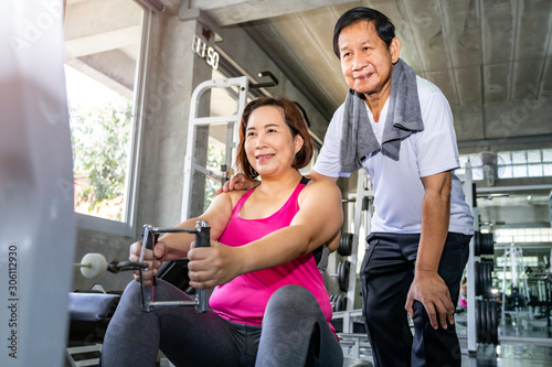 Asian senior couple smiling in sportswear exercising at gym.