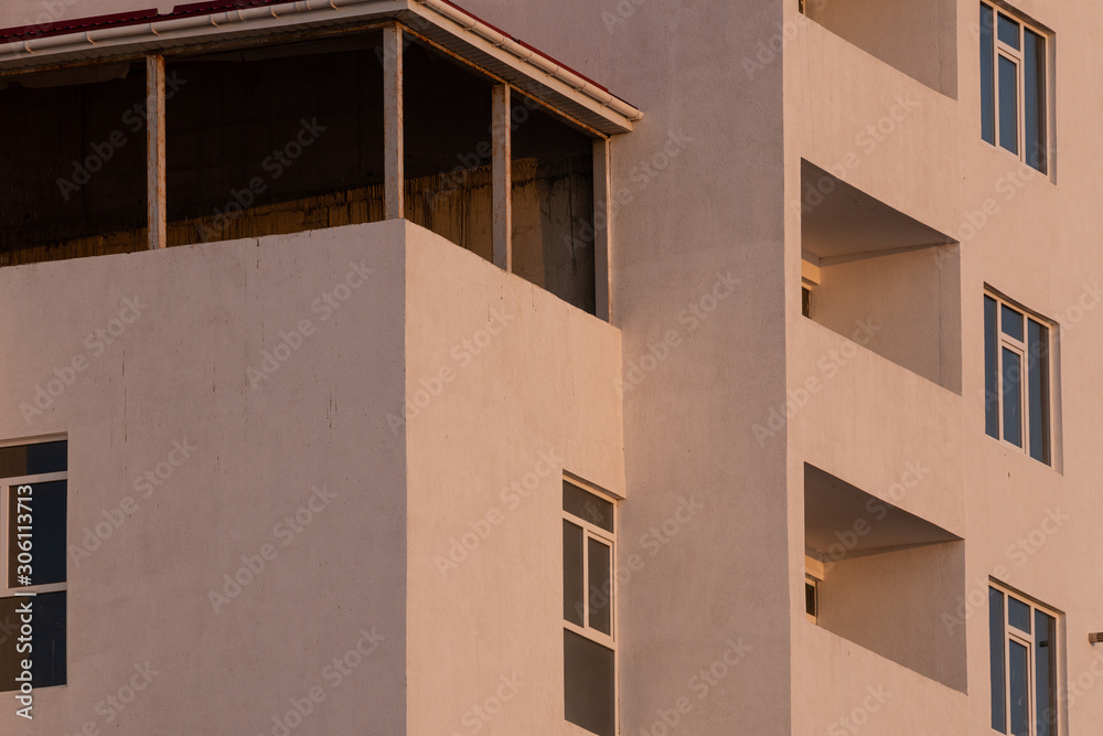 part of the white facade of the building with windows and balconies against a clear blue sky at sunrise and sunset part of the white facade of the building with windows and balconies against a clear blue sky at sunrise and sunset