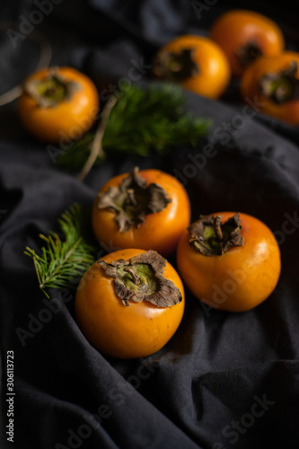 Ripe yellow persimmon with Christmas tree branches on a dark background. New Year's still life
