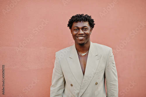 Stylish afro man in beige old school suit against pink wall. Fashionable young African male in casual jacket on bare torso.