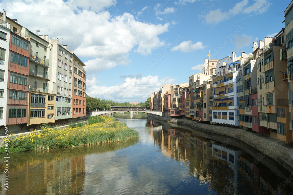 Girona, Rio Onyar. Medieval town, summers day. The old town houses by the river reflected in the still waters. Blue sky and nature and city in harmony. Colorful houses on the river bank.