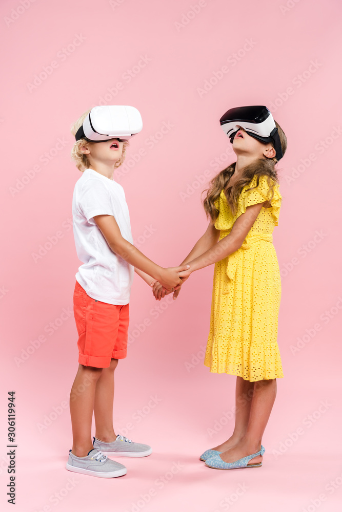 shocked kids with virtual reality headset holding hands on pink background