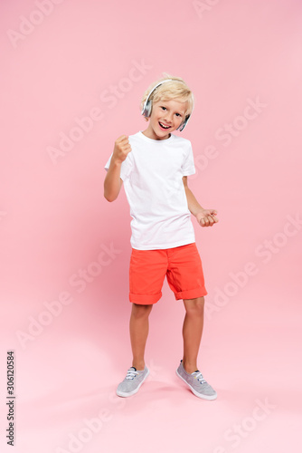 smiling kid with headphones listening music and dancing on pink background