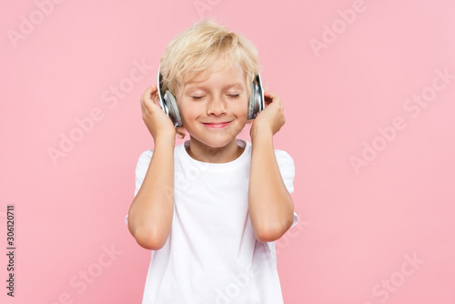 smiling kid with headphones listening music isolated on pink
