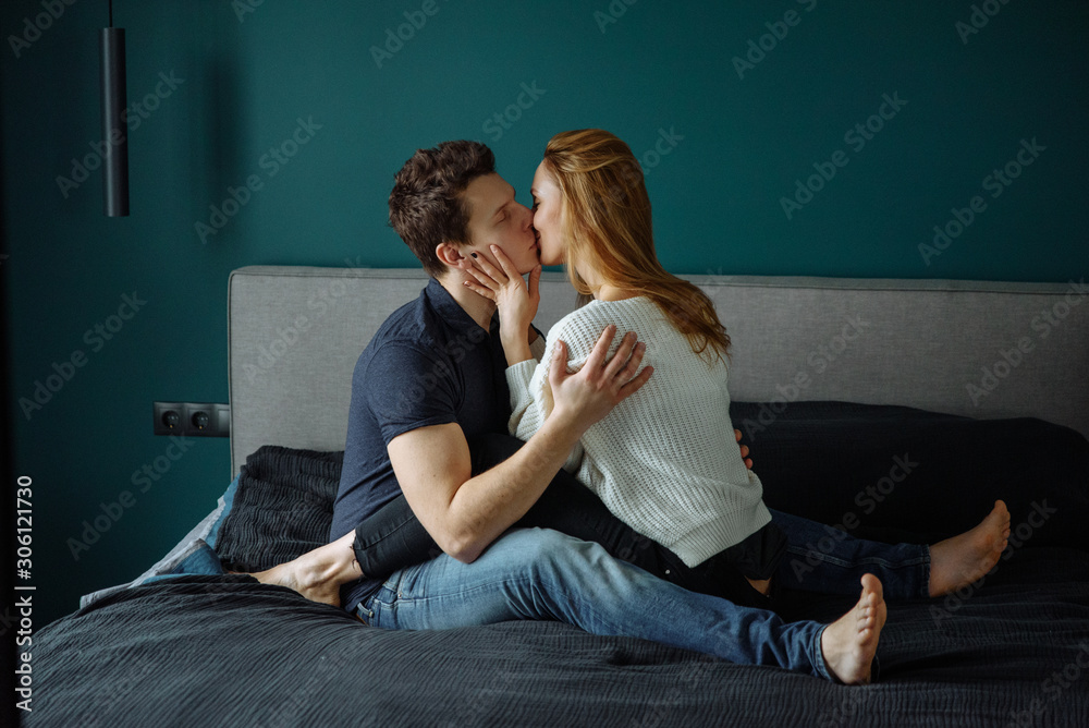Happy couple in love is hugging and kissing on the bed in the bedroom