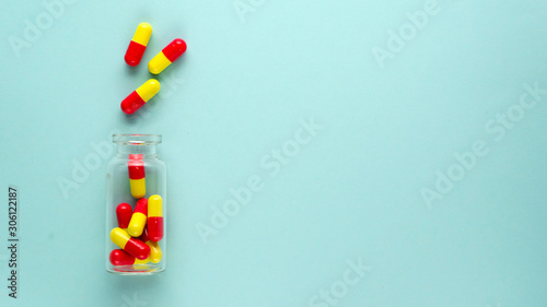 Bright red and yellow medicinal capsules in glass transparent bottle on a light blue background. Health care concept. Flat lay, top view. Copy space