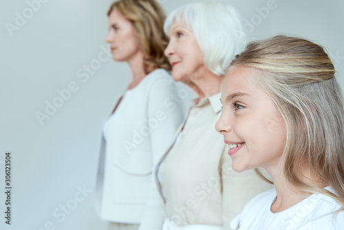 selective focus of smiling granddaughter and grandmother, mother on background isolated on grey