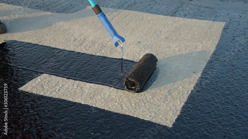 Waterproofing coating. Worker applies bitumen mastic on the foundation. Roofer cover the rooftop polymer modified bitumen waterproofing primer, with a roller brush.