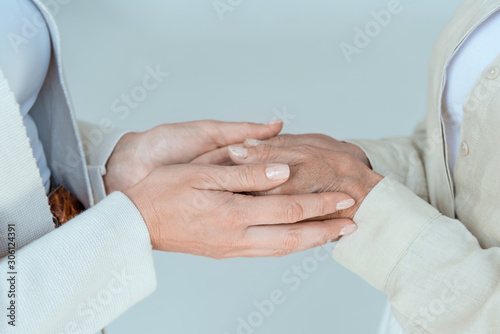 cropped view of mother and daughter holding hands isolated on grey