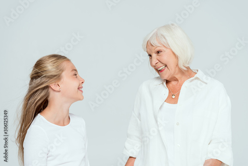 smiling granddaughter and grandmother looking at each other isolated on grey
