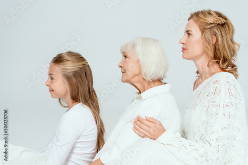 side view of smiling granddaughter, mother and grandmother hugging isolated on grey
