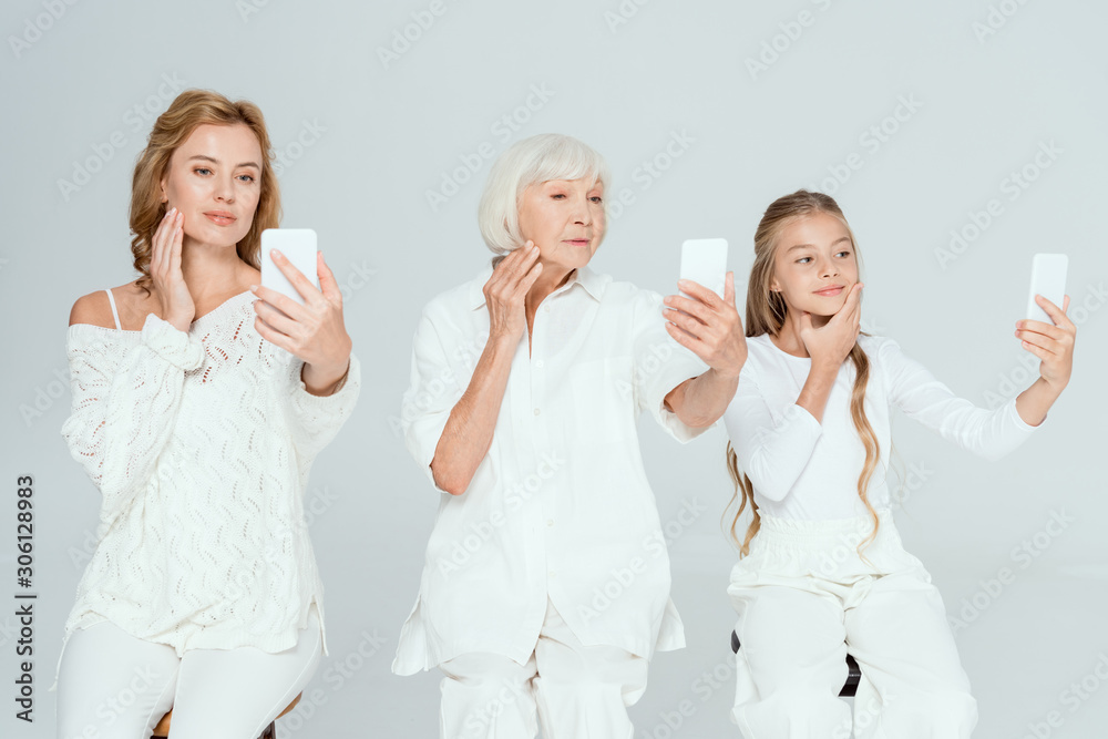 smiling granddaughter, mother and grandmother taking selfies and touching faces isolated on grey smiling granddaughter, mother and grandmother taking selfies and touching faces isolated on grey