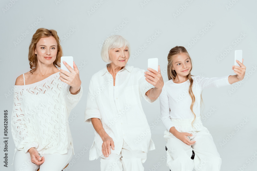 smiling granddaughter, mother and grandmother taking selfies isolated on grey smiling granddaughter, mother and grandmother taking selfies isolated on grey