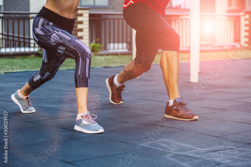 fitness, sport, exercise, lifestyle concept. Mixed race young man and woman doing exercise on street sports ground. Team of two athletes exercising lunges while having sports training in the morning. © Iryna