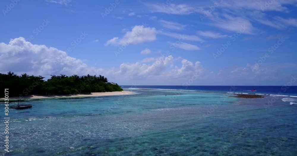 Vivid colors of blue azure lagoon with white waves washing exotic beach under lush vegetation of island and light blue sky with white clouds in Bahamas Vivid colors of blue azure lagoon with white waves washing exotic beach under lush vegetation of island and light blue sky with white clouds in Bahamas