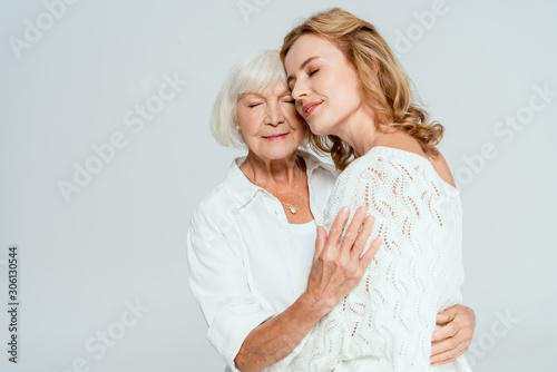 attractive daughter with closed eyes hugging mother isolated on grey