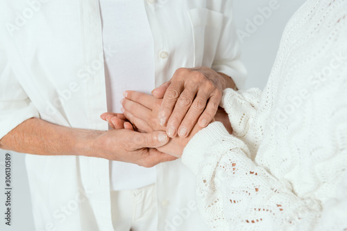 Billede på lærred cropped view of mother and daughter holding hands isolated on grey