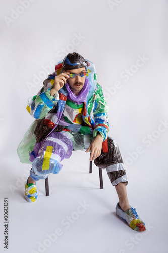 Man wearing plastic on white background. Male model in clothes made of garbage. Fashion, style, recycling, eco and environmental concept. Too much pollution, we're eating and taking it. Waste products