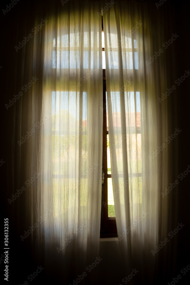 Window of an old house with curtains that let in a beautiful light.