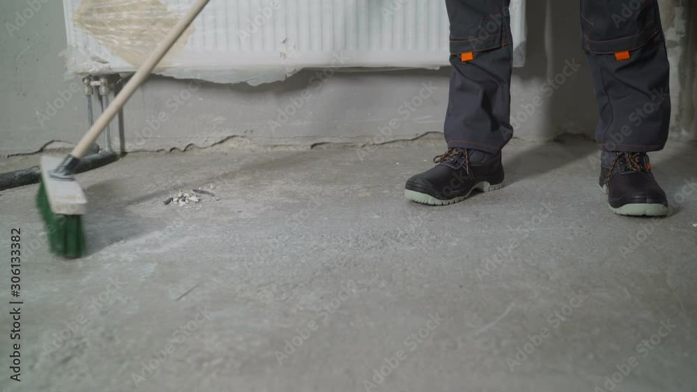 A worker is cleaning a concrete floor. Preparing the floor for cover. The hand of a working man holds a broom, sweeping the concrete floor. A worker is cleaning a concrete floor. Preparing the floor for cover. The hand of a working man holds a broom, sweeping the concrete floor.