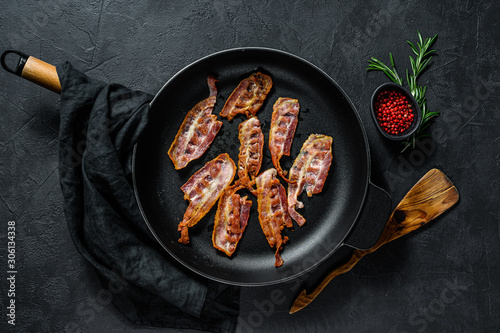 Cooked sizzling hot tasty crispy bacon on a skillet. Farm organic meat. Black background. Top view