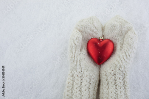 Female hands in mittens with red heart on white snow background