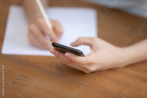 Young woman sitting holding smartphone with blurred background close up.